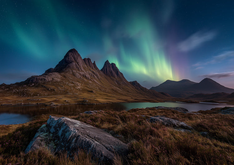 Green and violet northern lights over a dark Highland peak and still loch