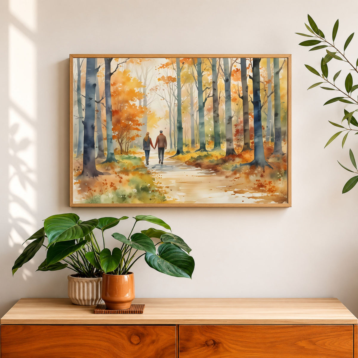 Autumn Walk for Two, in a natural wood frame above a wooden sideboard with potted plants on a sunlit cream wall