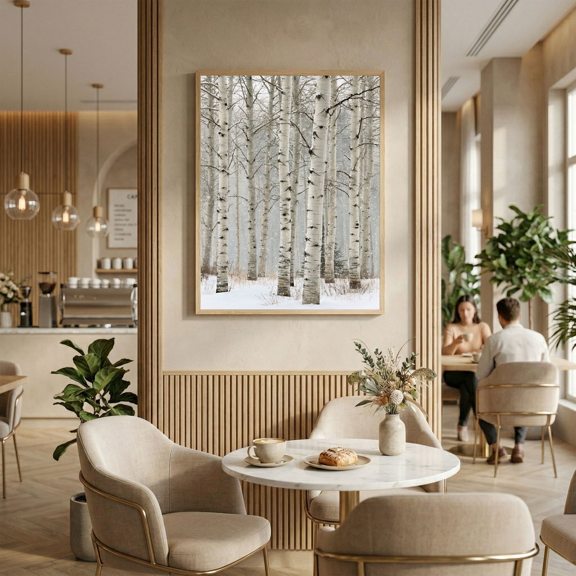 Birch in falling snow, in a light wood frame above fluted panelling in a warm neutral cafe