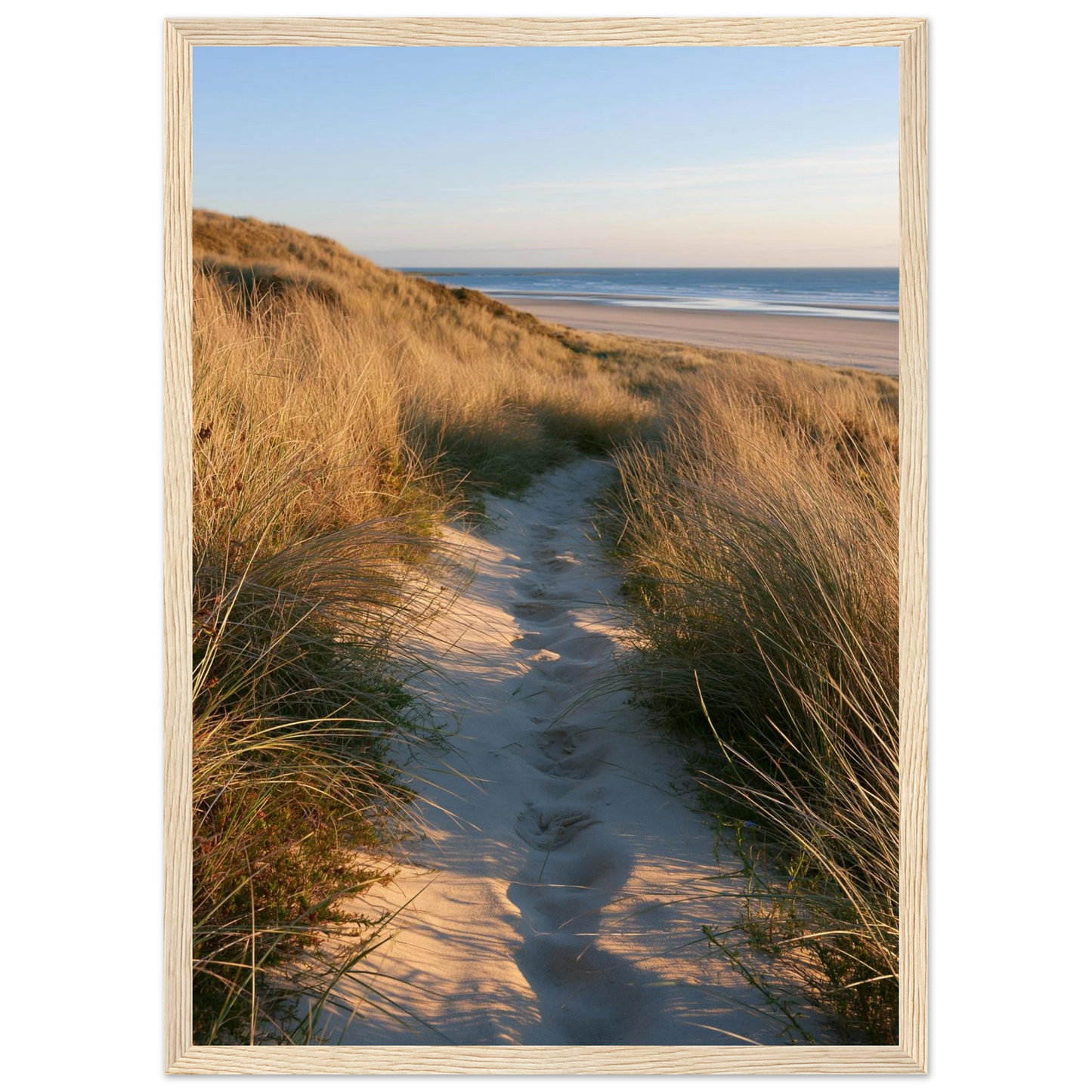 Sand track through amber marram grass to an empty beach at golden hour, print in a natural light wood frame
