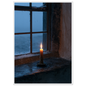 Candle burning on a stone windowsill at blue dusk, print in a white frame