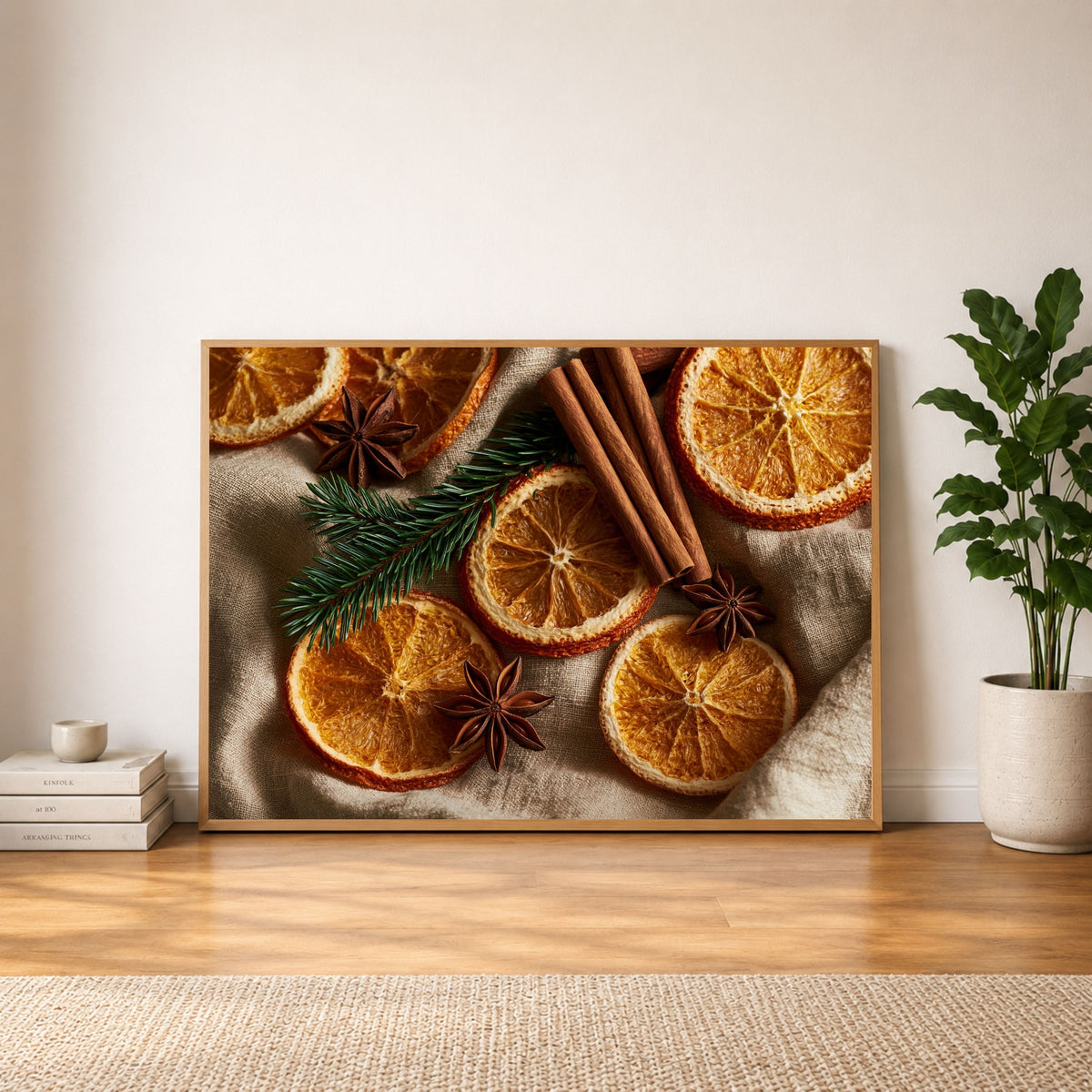 Dried oranges, cinnamon and star anise on linen, in a light wood frame leaning against a plain wall beside a potted plant