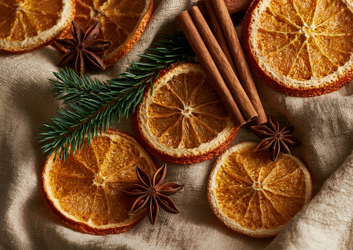 Dried orange slices, cinnamon sticks, star anise and a sprig of spruce arranged on crumpled natural linen, seen from directly above