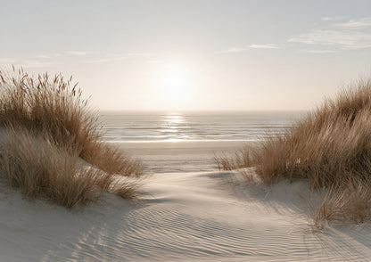A sandy path winding between marram-grassed dunes to a bright band of sea under a low, hazy sun