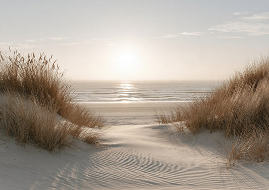 A sandy path winding between marram-grassed dunes to a bright band of sea under a low, hazy sun