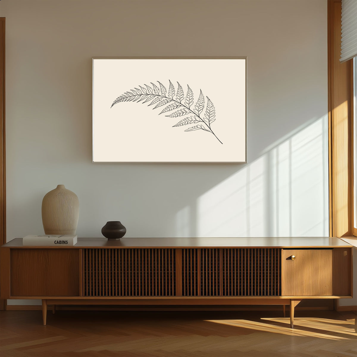 Fern frond line drawing on warm cream, print in a slim oak frame above a walnut sideboard in warm afternoon light