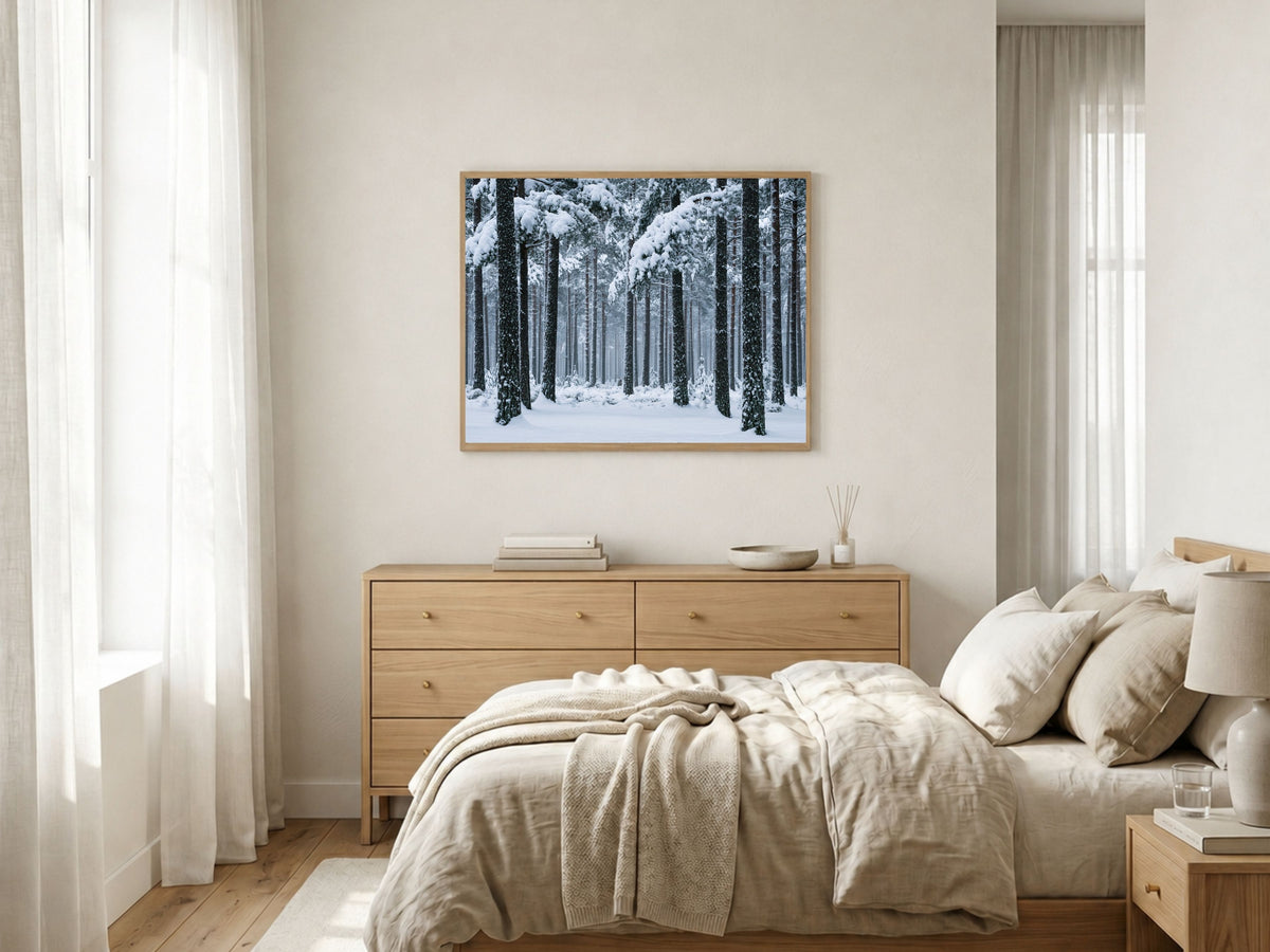Snowy pine forest print in a light wood frame above a chest of drawers in a bright neutral bedroom