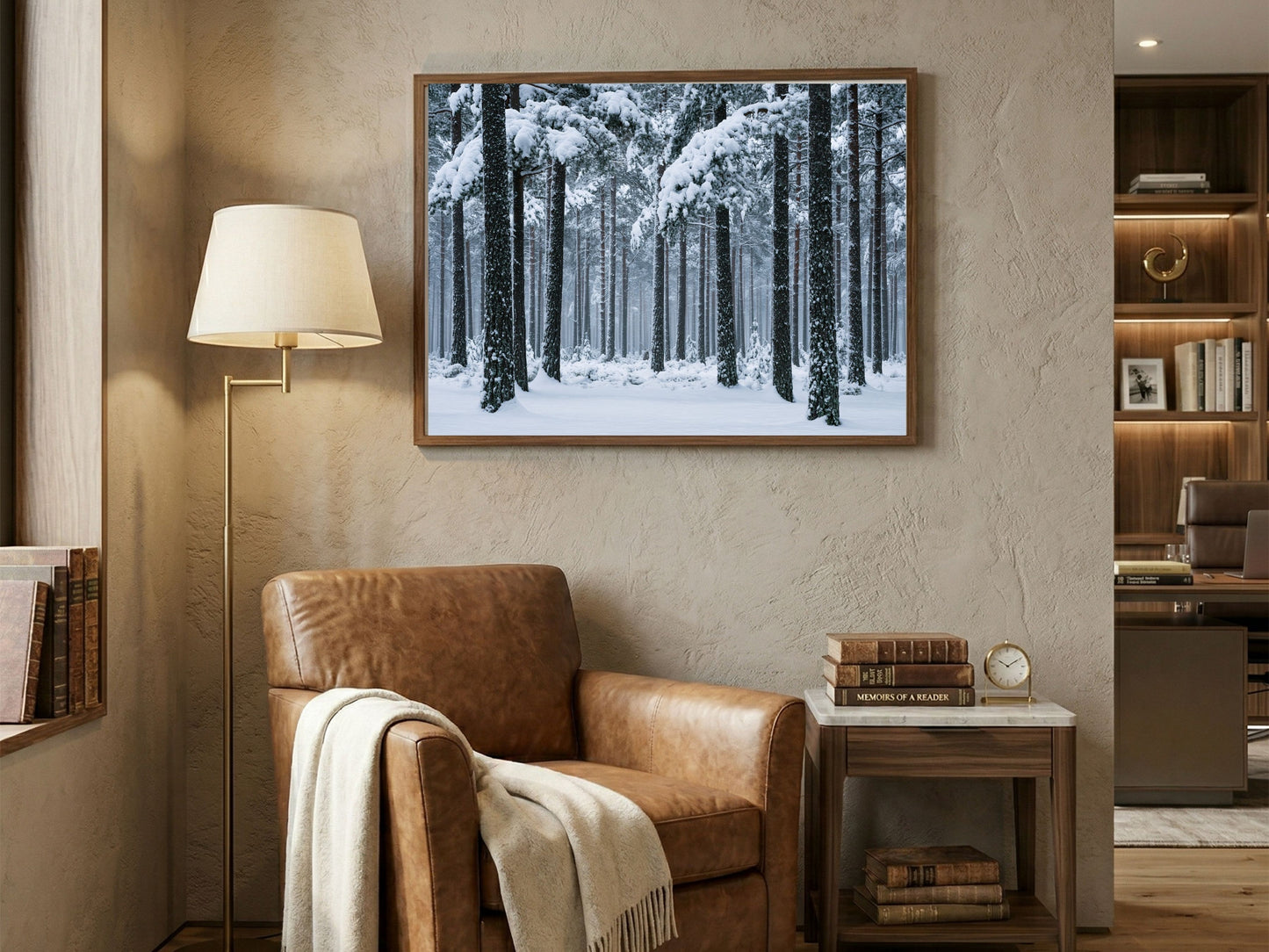 Snowy pine forest print in a wood frame above a tan leather armchair in a warm reading corner