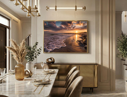 Beach at sunset with breaking waves and a low sun, framed in light wood in an elegant dining room with a marble table
