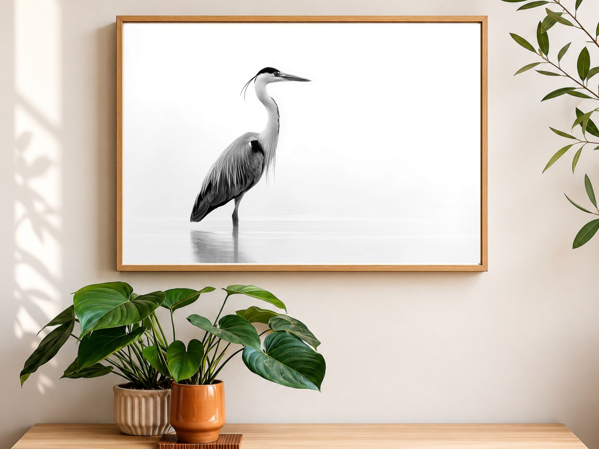 Black and white grey heron in still water, framed in light wood above a console table with houseplants