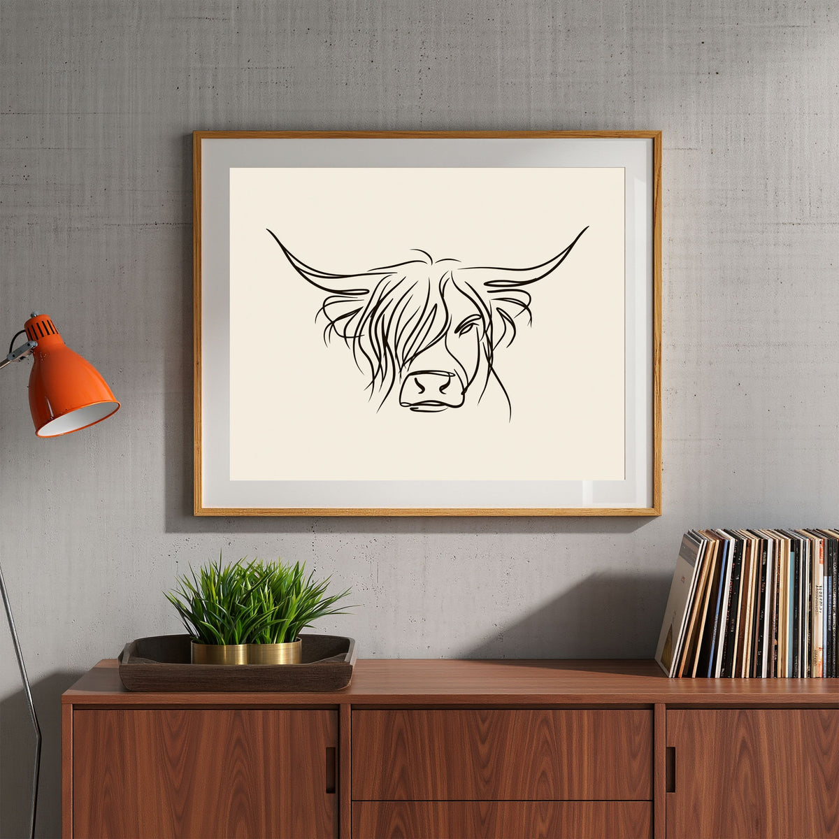 Minimal line drawing of a Highland cow, in a light wood frame above a walnut sideboard with a plant and vinyl in a living room
