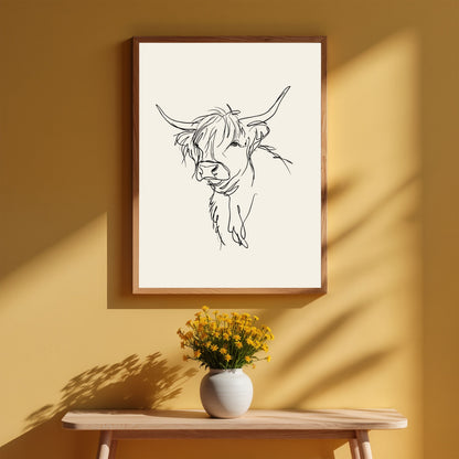 Loose line sketch of a Highland cow, in a light wood frame on a warm ochre wall above a bench with a vase of yellow flowers