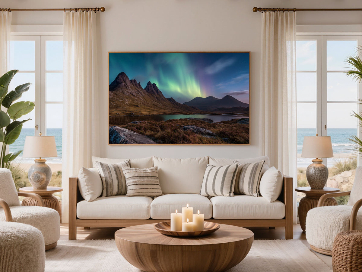 Northern lights over a Highland loch and mountain, in a dark frame above a white sofa in a coastal living room