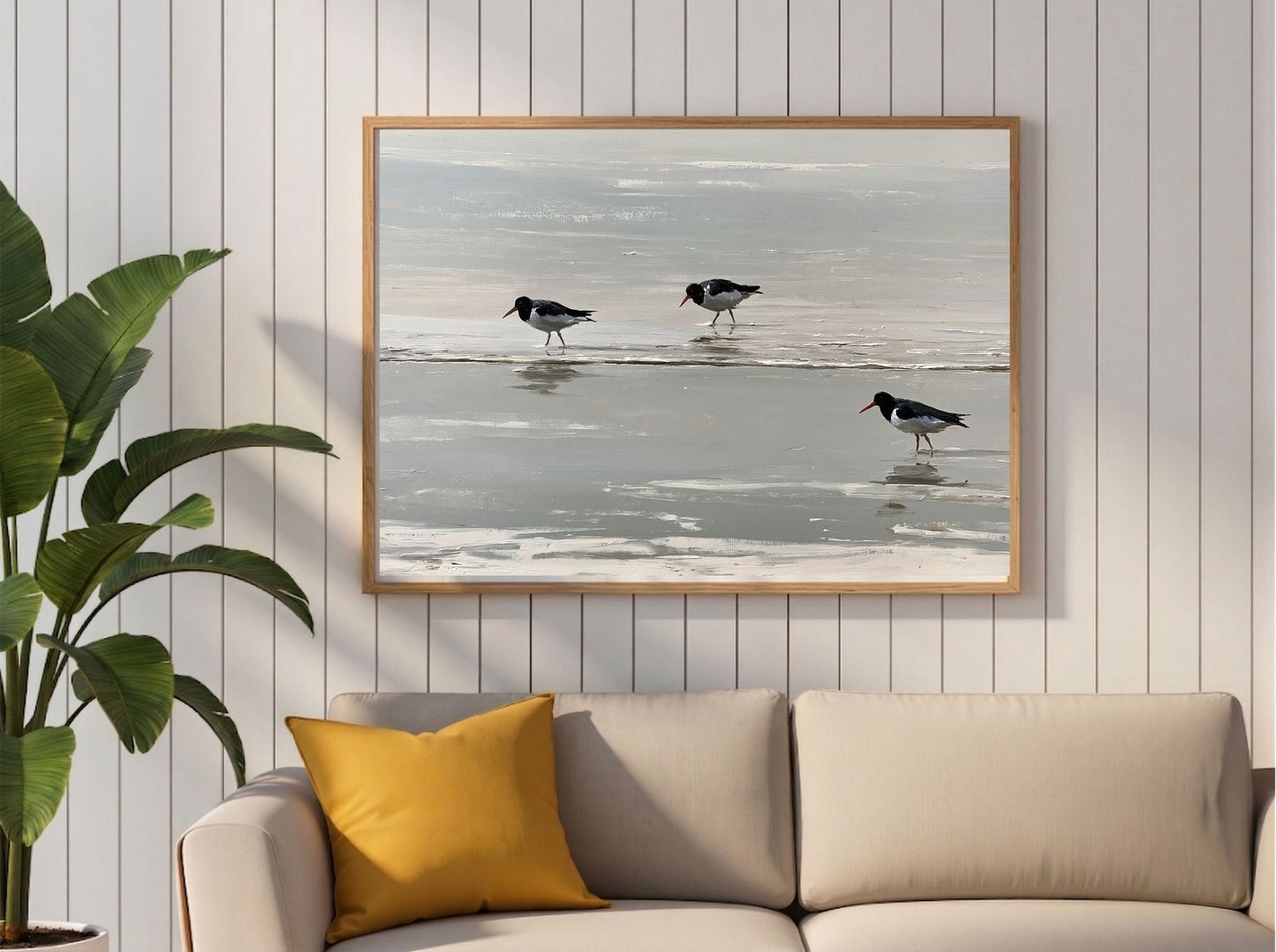 Three oystercatchers on the tideline, framed in light wood on a panelled wall above a cream sofa