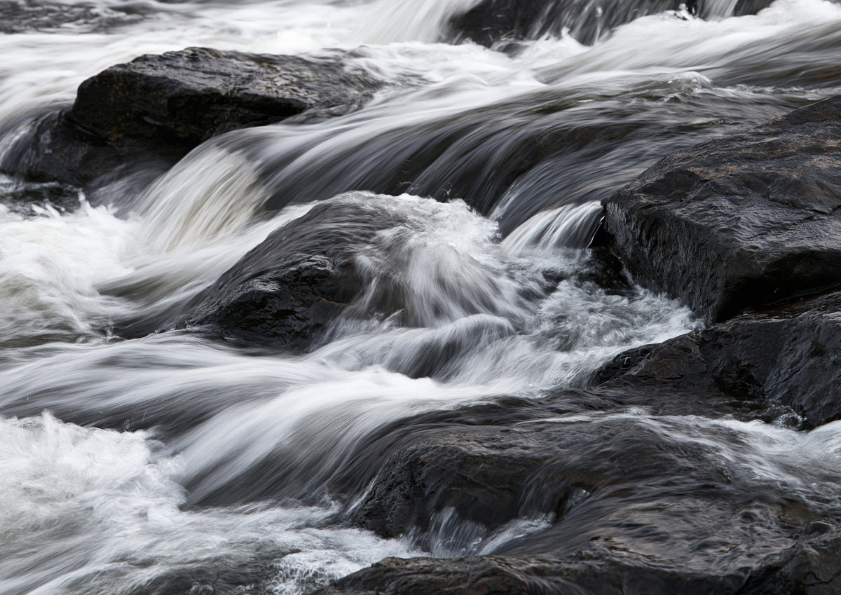 Pale water pouring over near-black wet rock, the flow smoothed into long soft streaks like silk laid over stone