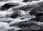 Pale water pouring over near-black wet rock, the flow smoothed into long soft streaks like silk laid over stone