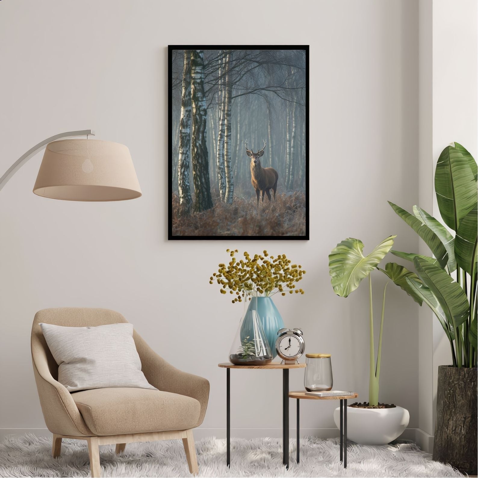 Red deer stag in a misty birch wood, in a black frame above an armchair and side tables in a plant-filled reading corner