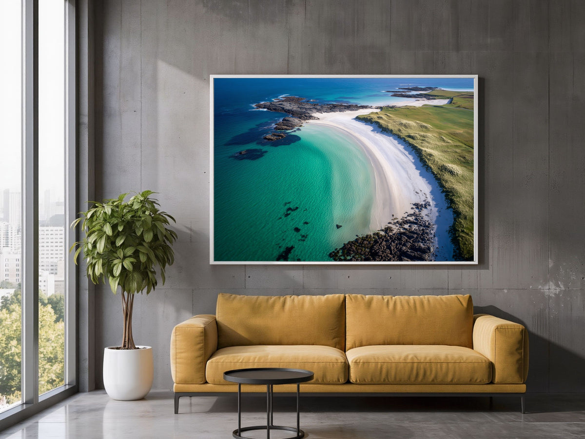 Turquoise bay and white shell-sand beach from the air, in a white frame above a mustard sofa in a loft living room