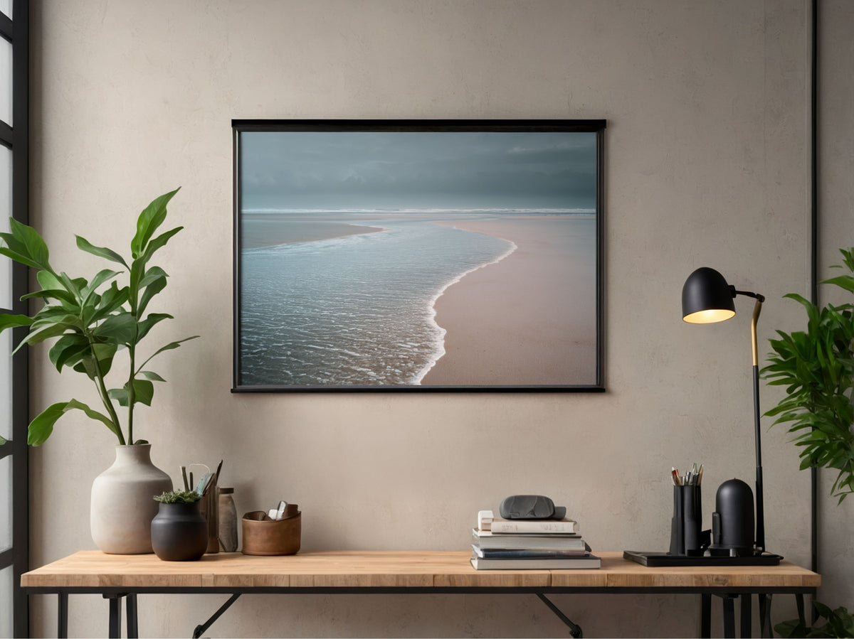 Pale sea washing over an empty beach at low tide, in a black frame above a desk in a home office
