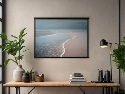 Pale sea washing over an empty beach at low tide, in a black frame above a desk in a home office