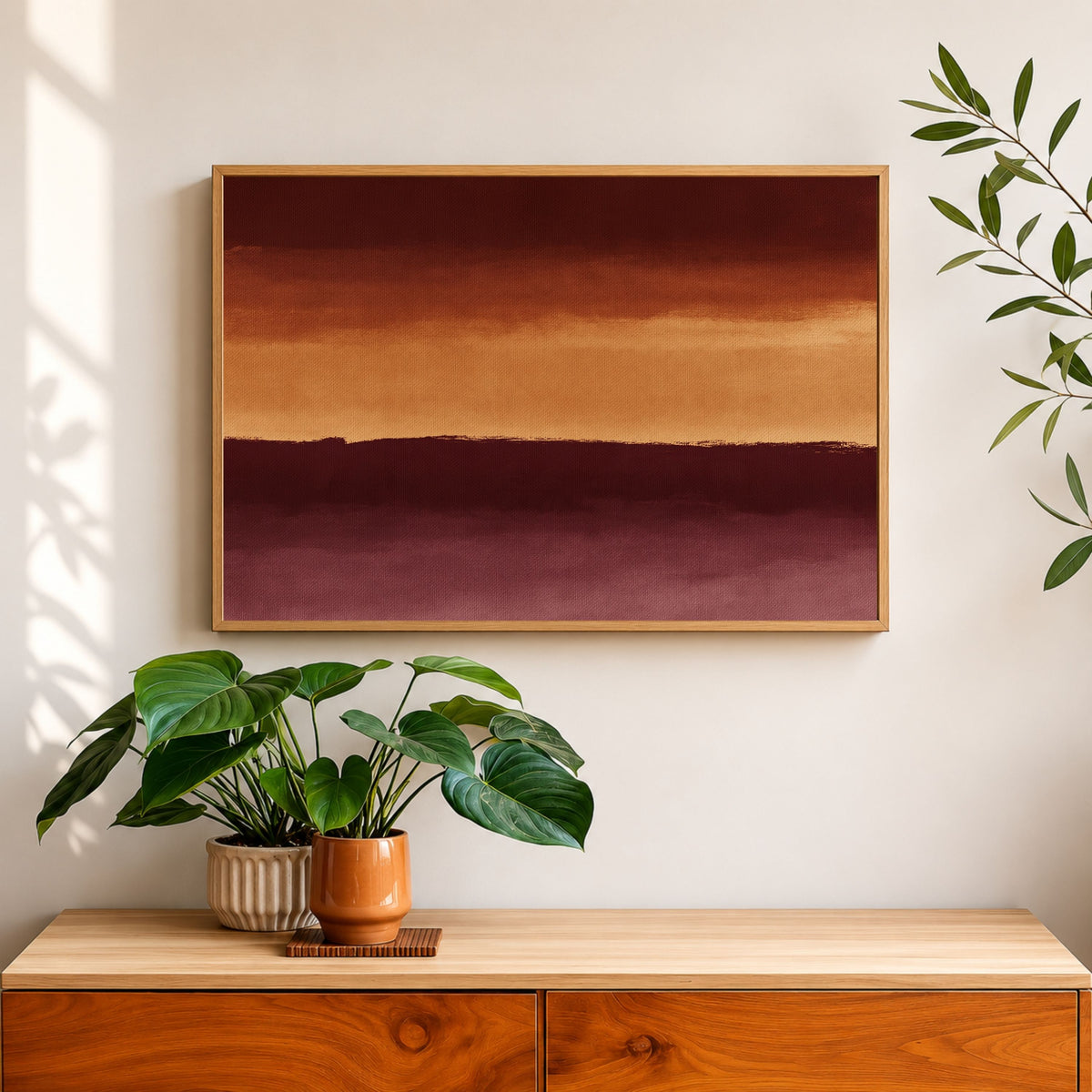 Three bands in rust and ochre, in a light wood frame above a walnut sideboard with a trailing plant