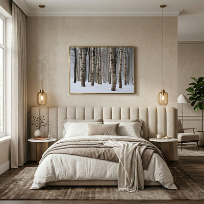 Winter birch wood in snow, in a pale wood frame above a cream upholstered bed in a warm neutral bedroom