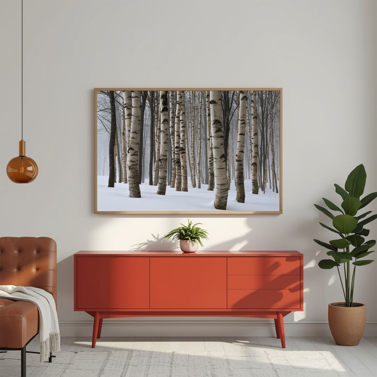 Winter birch wood in snow, in a pale wood frame above a red mid-century sideboard in a bright living room